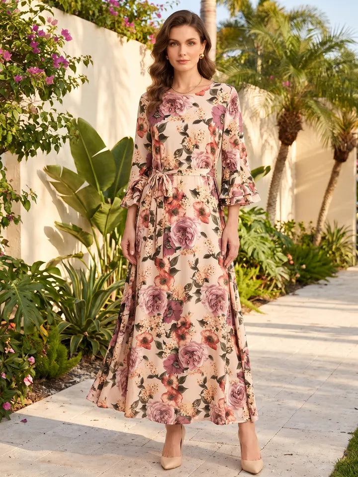 A woman in a cream floral maxi dress with bell sleeves and a tie belt in a sunny garden
